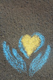 Photo of Heart with hands drawn with blue and yellow chalks on asphalt outdoors, top view