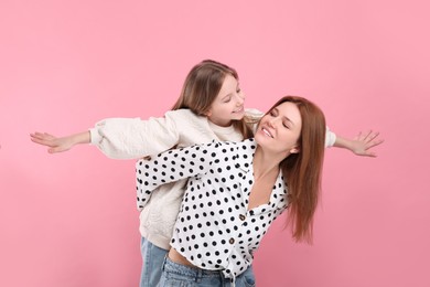 Happy mother with her cute daughter on pink background