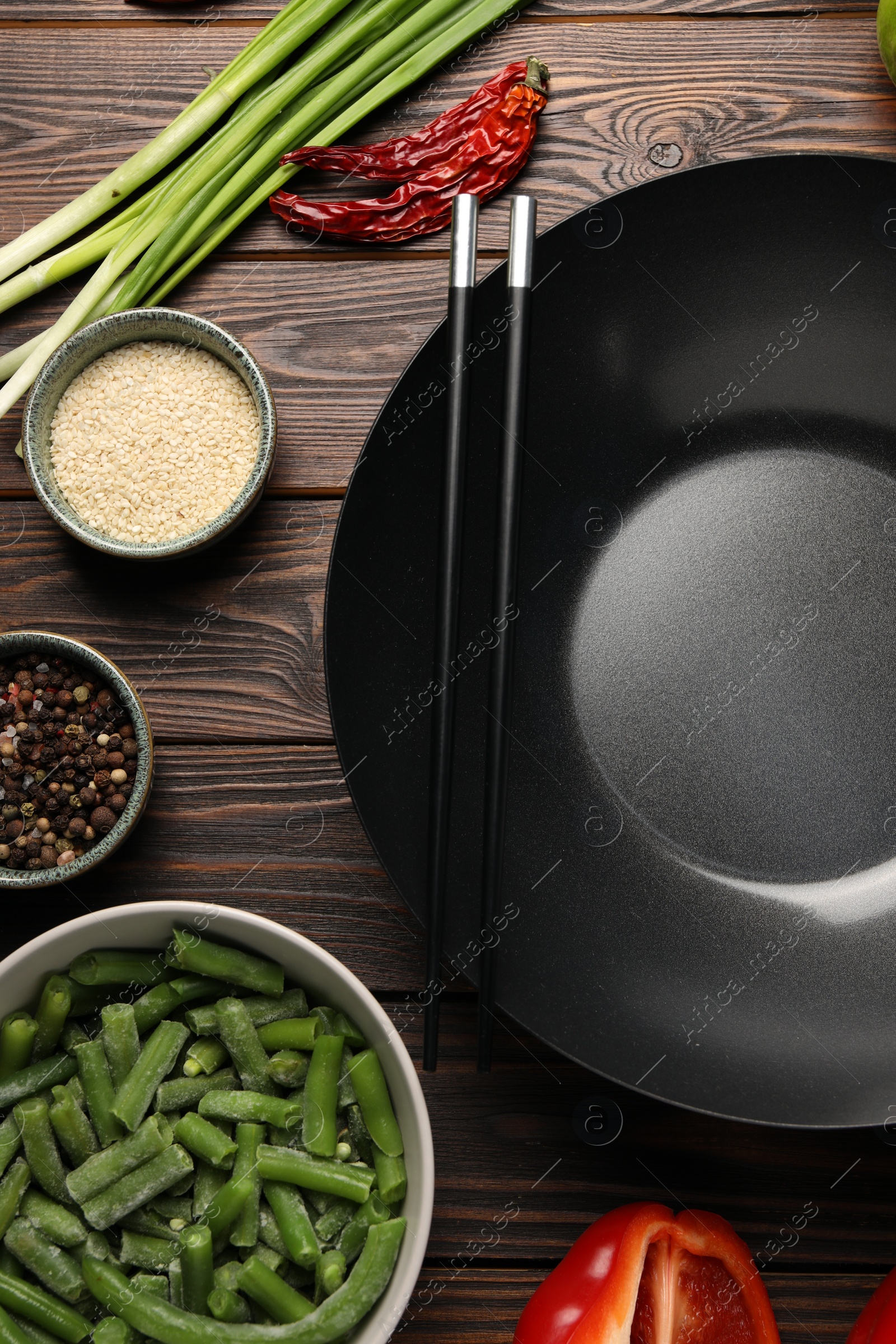 Photo of Black wok, chopsticks and products on wooden table, flat lay