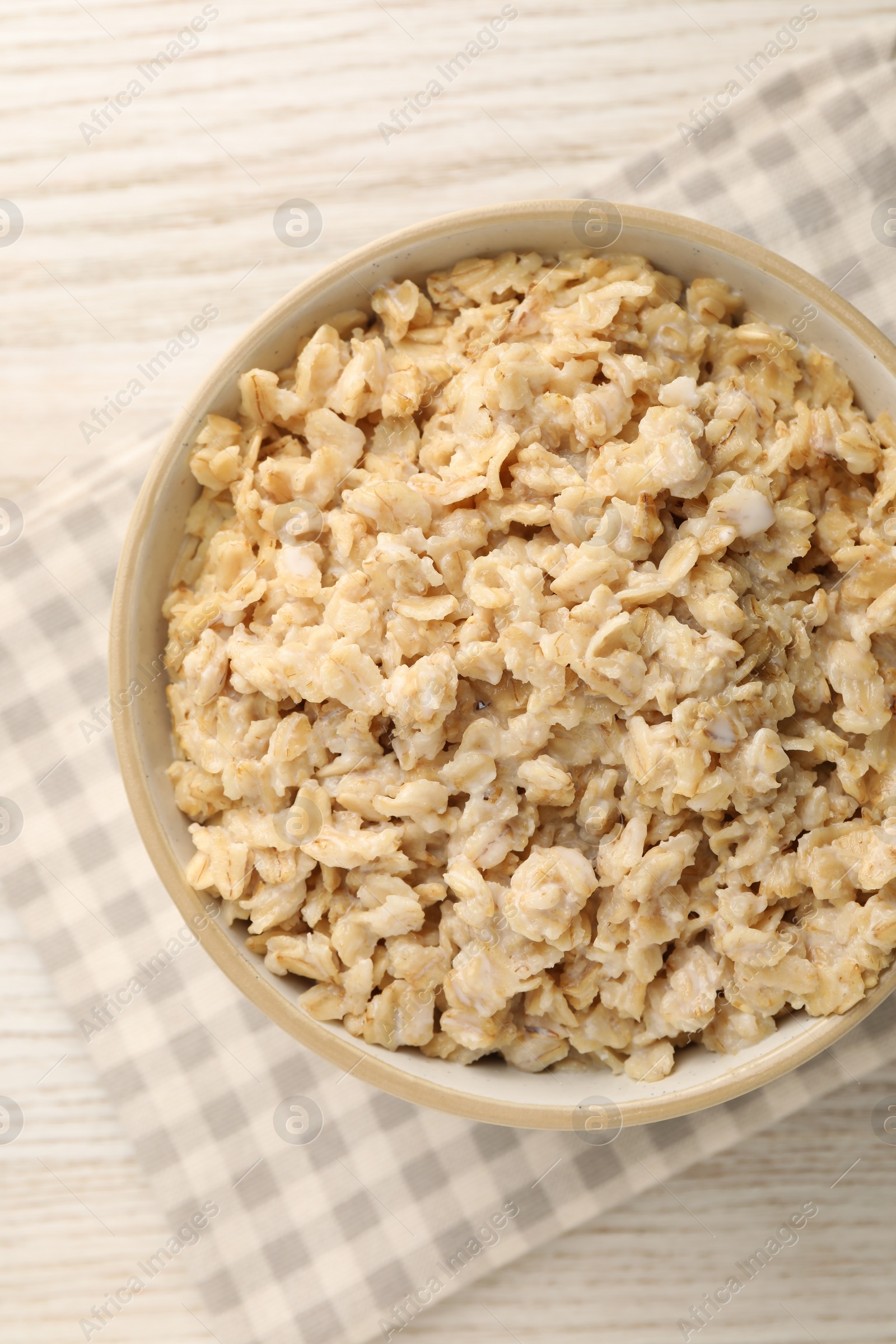 Photo of Tasty boiled oatmeal in bowl on light wooden table, top view