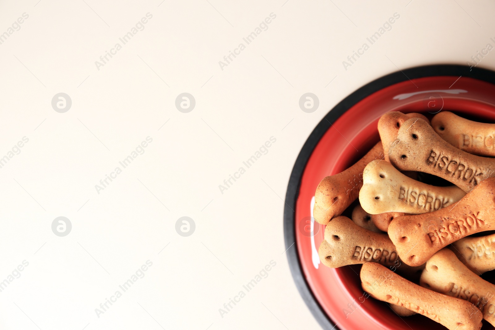 Photo of Bone shaped dog cookies in feeding bowl on beige table, top view. Space for text