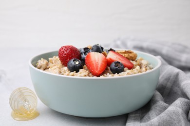 Photo of Tasty oatmeal with strawberries, blueberries and walnuts in bowl on grey table