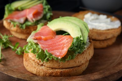 Photo of organic rusks with salmon, cream cheese and avocado served on wooden board, closeup