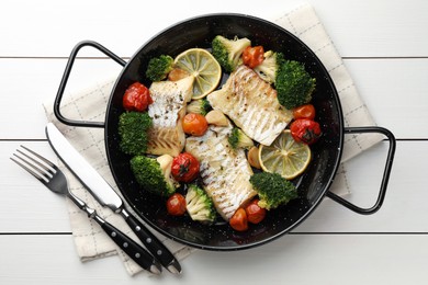 Photo of Tasty cod cooked with vegetables in frying pan and cutlery on white wooden table, flat lay