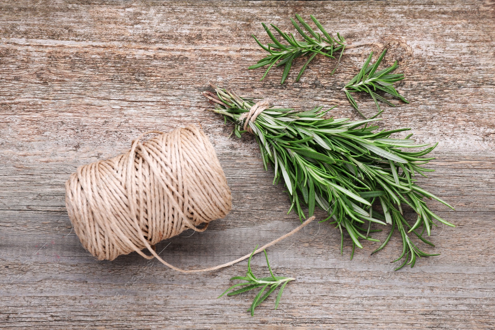 Photo of Sprigs of fresh rosemary and twine on wooden table, flat lay