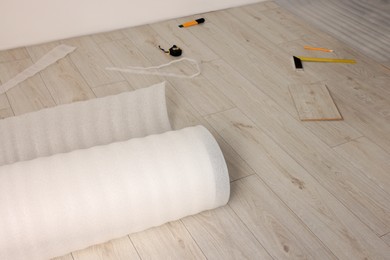 Photo of Roll of polyethylene foam and different tools on laminated floor in room