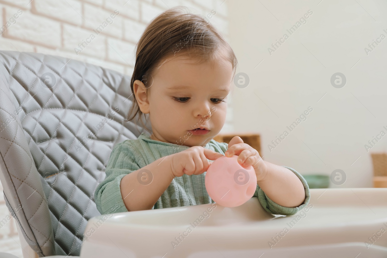 Photo of Cute little baby nibbling toy in high chair indoors