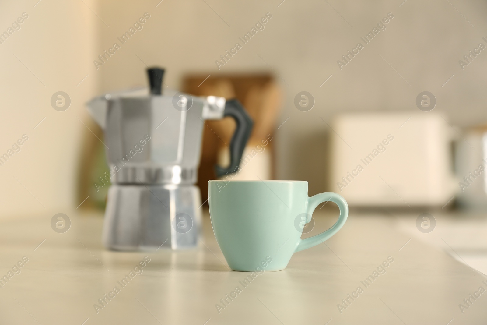 Photo of Cup of coffee and moka pot on light table in kitchen, selective focus