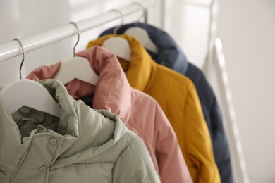 Photo of Different warm jackets hanging on rack indoors, closeup