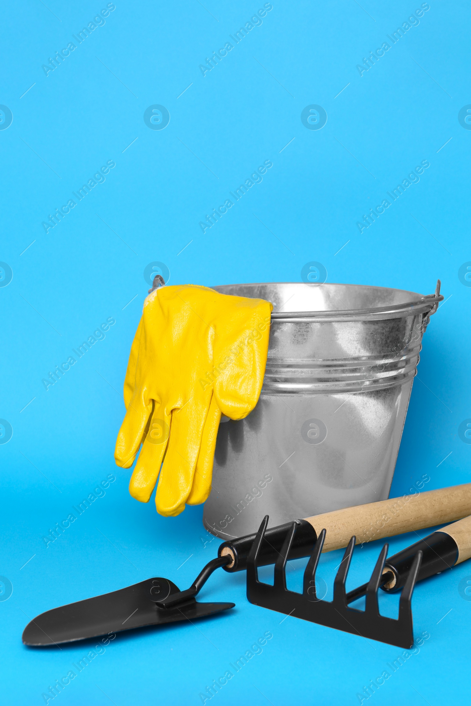 Photo of Gardening gloves, tools and bucket on light blue background