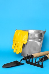 Gardening gloves, tools and bucket on light blue background
