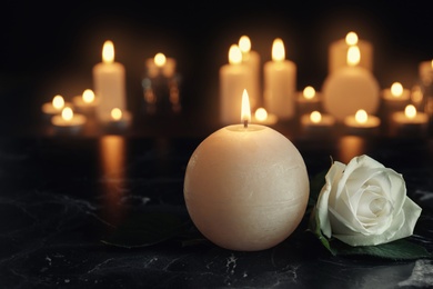 Photo of White rose and burning candle on table in darkness, space for text. Funeral symbol