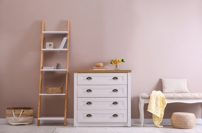 Photo of Elegant room interior with stylish chest of drawers, shelving unit and comfortable bench