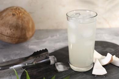 Photo of Glass of coconut water, ice cubes and nuts on grey table