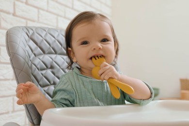 Photo of Cute little baby nibbling cutlery in high chair indoors