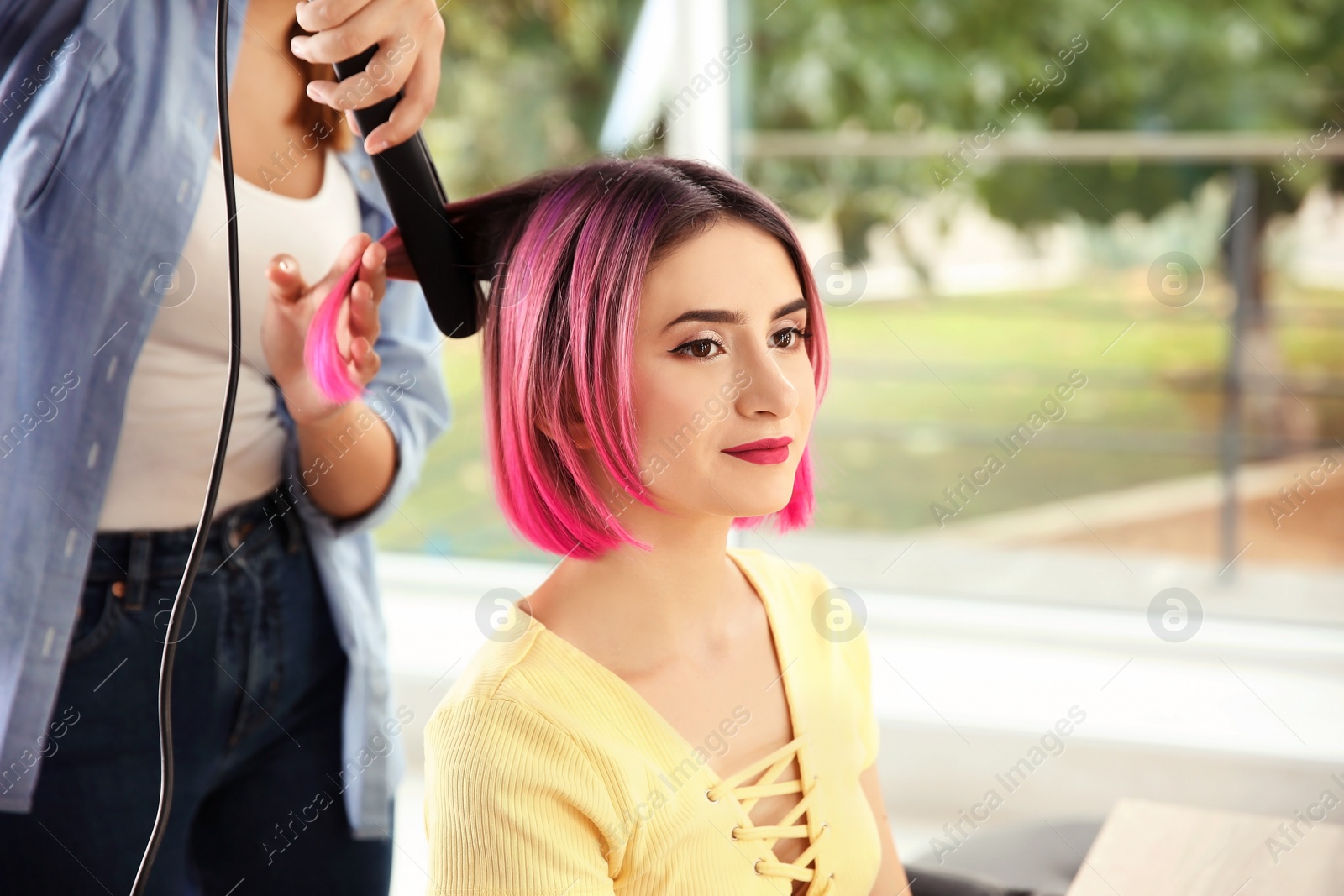 Photo of Professional hairdresser working with young woman in beauty salon. Trendy hair color