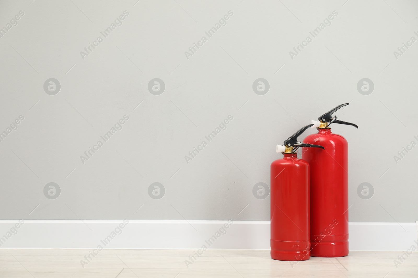 Photo of Fire extinguishers on floor near light grey wall, space for text