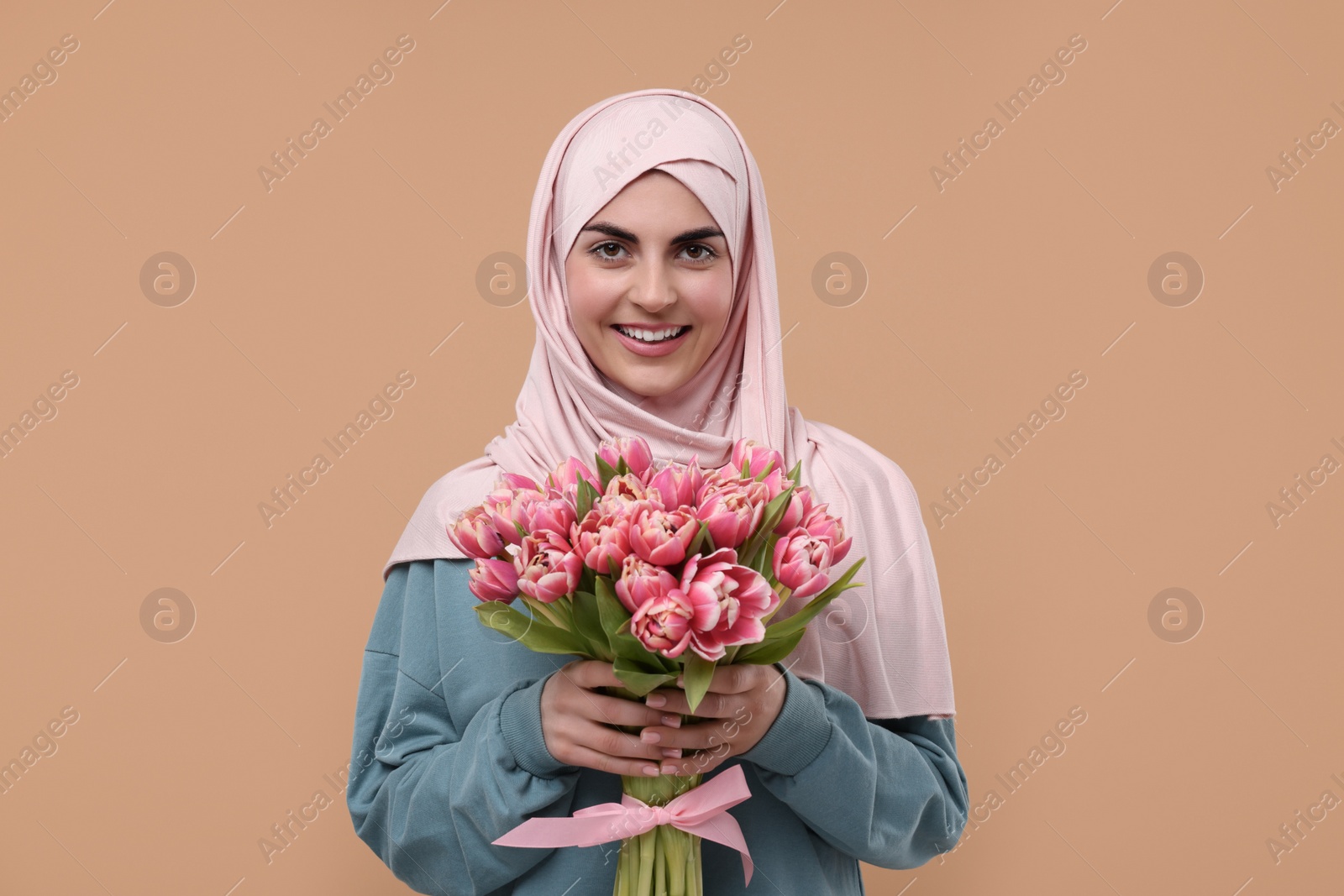 Photo of Happy woman in hijab with beautiful bouquet on beige background