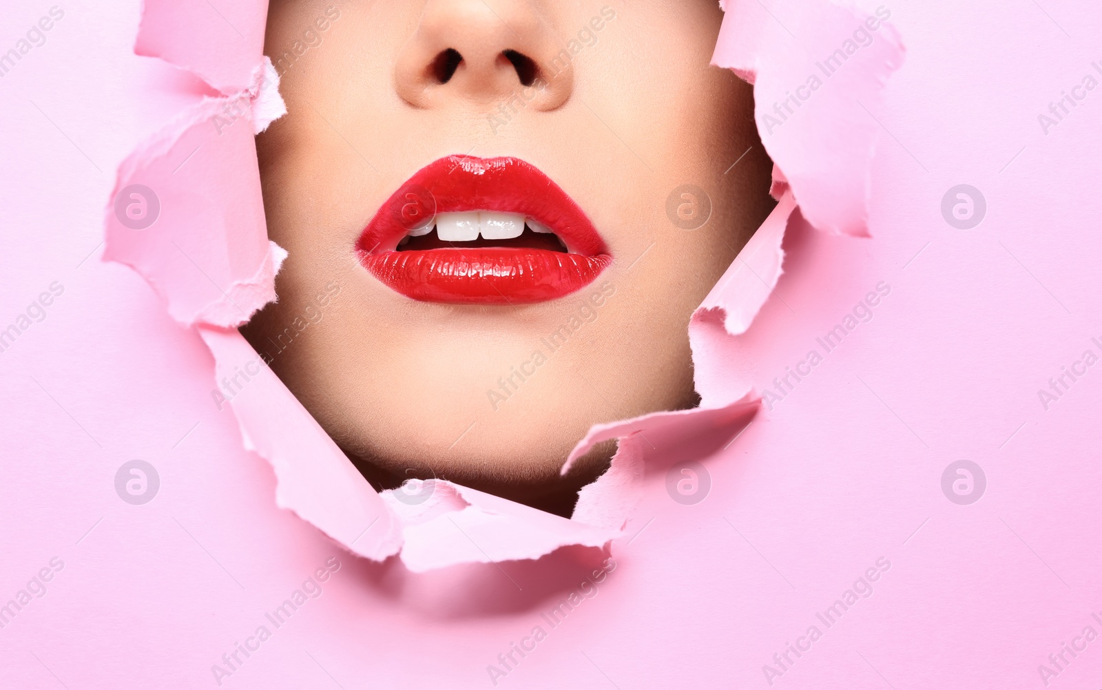 Photo of View of beautiful young woman with red lips through hole in color paper, closeup