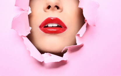 Photo of View of beautiful young woman with red lips through hole in color paper, closeup