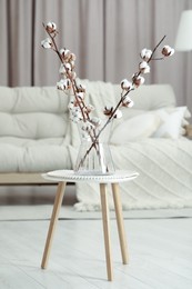 Branches with white fluffy cotton flowers on coffee table in cozy room. Interior design