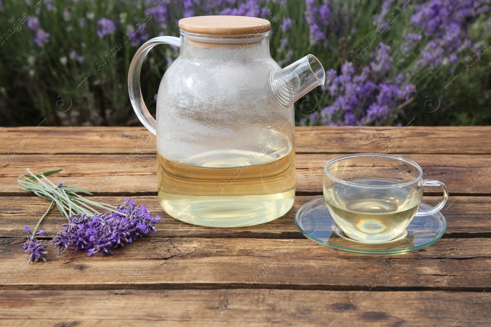 Photo of Tasty herbal tea and fresh lavender flowers on wooden table in field