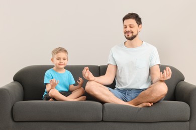 Photo of Father with son meditating together on sofa at home. Harmony and zen