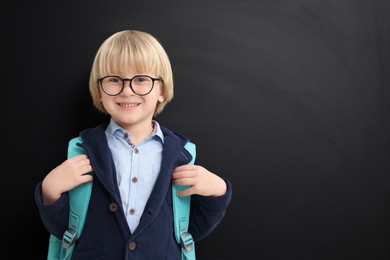 Happy little school child with backpack near chalkboard. Space for text