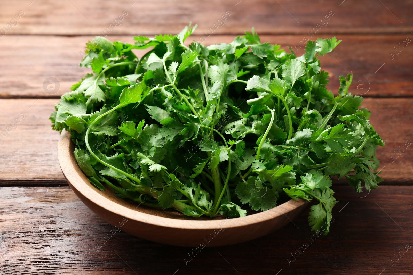 Photo of Fresh coriander in bowl on wooden table, closeup