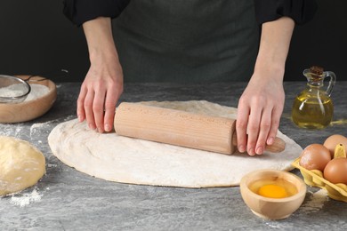 Woman rolling raw dough at grey table, closeup