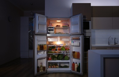 Photo of Open refrigerator filled with food in kitchen at night