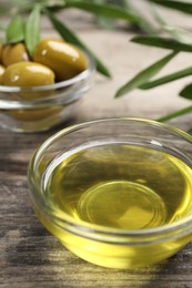 Photo of Cooking oil and olives on wooden table, closeup