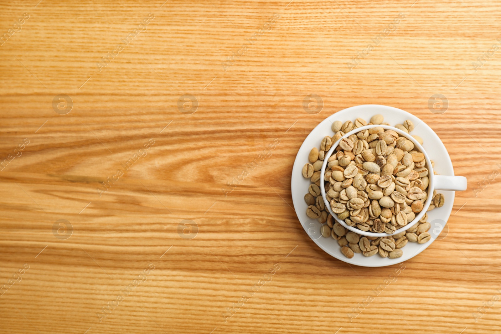 Photo of Cup and saucer with green coffee beans on wooden background, top view. Space for text