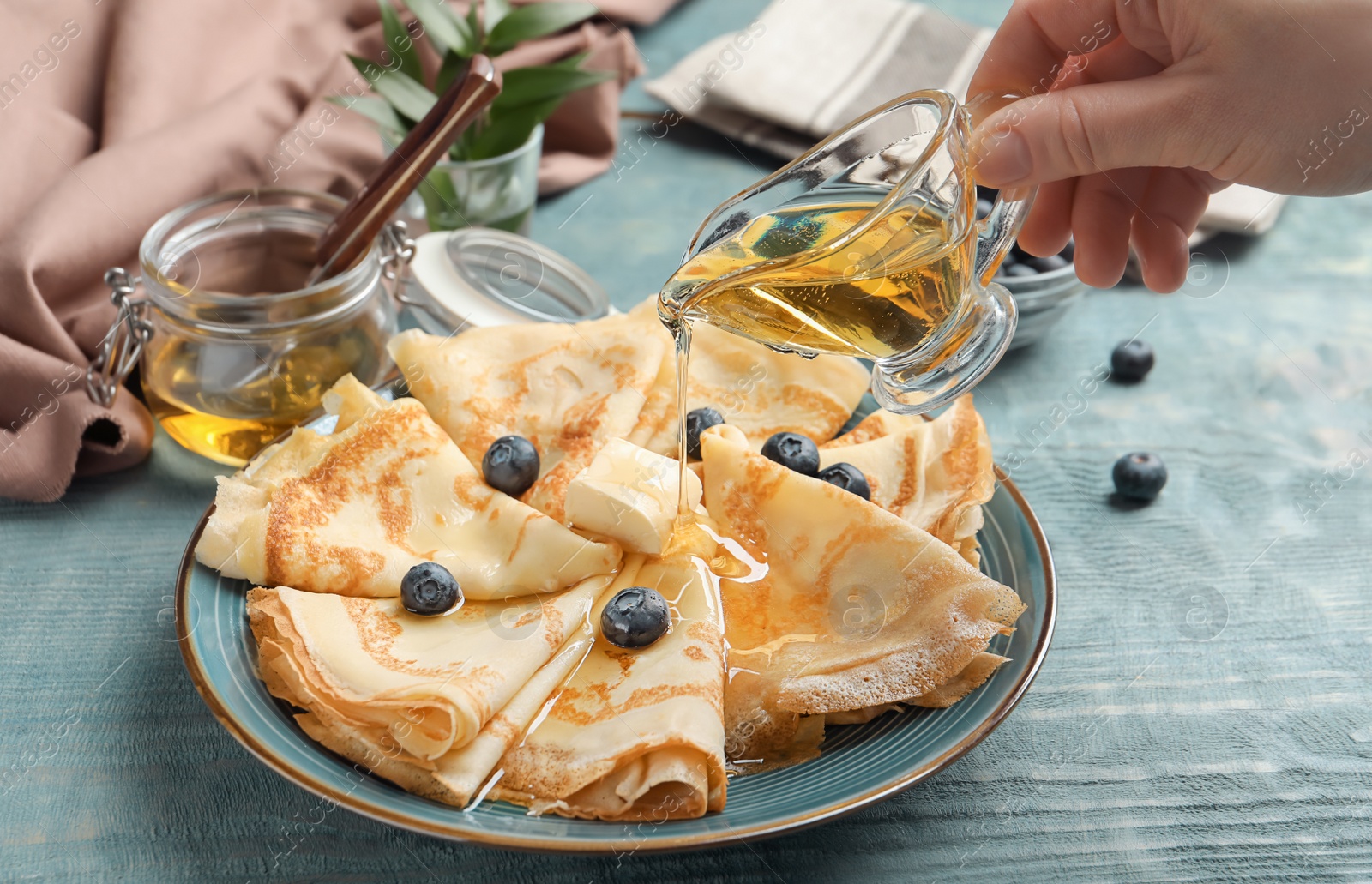 Photo of Woman pouring honey on thin pancakes with berries and butter, closeup