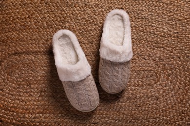 Photo of Pair of warm stylish slippers on wicker carpet, top view