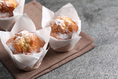 Photo of Delicious muffins with powdered sugar on grey table, closeup