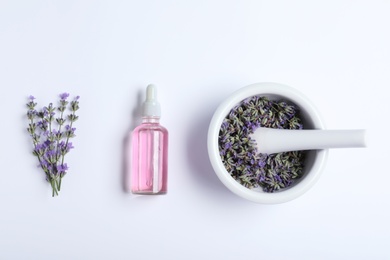 Photo of Bottle of essential oil, mortar and pestle with lavender flowers on white background, flat lay