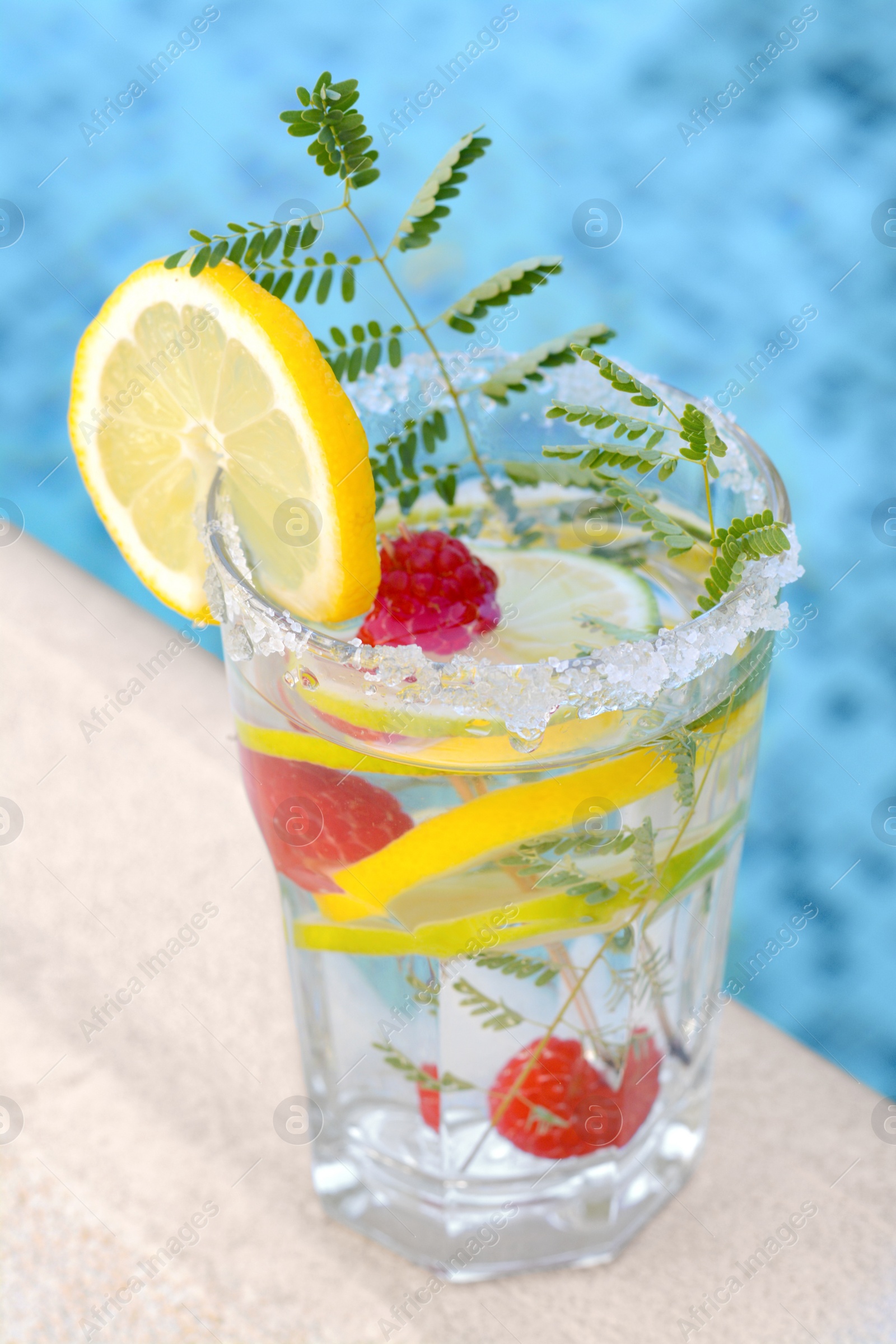 Photo of Delicious refreshing lemonade with raspberries near swimming pool, closeup