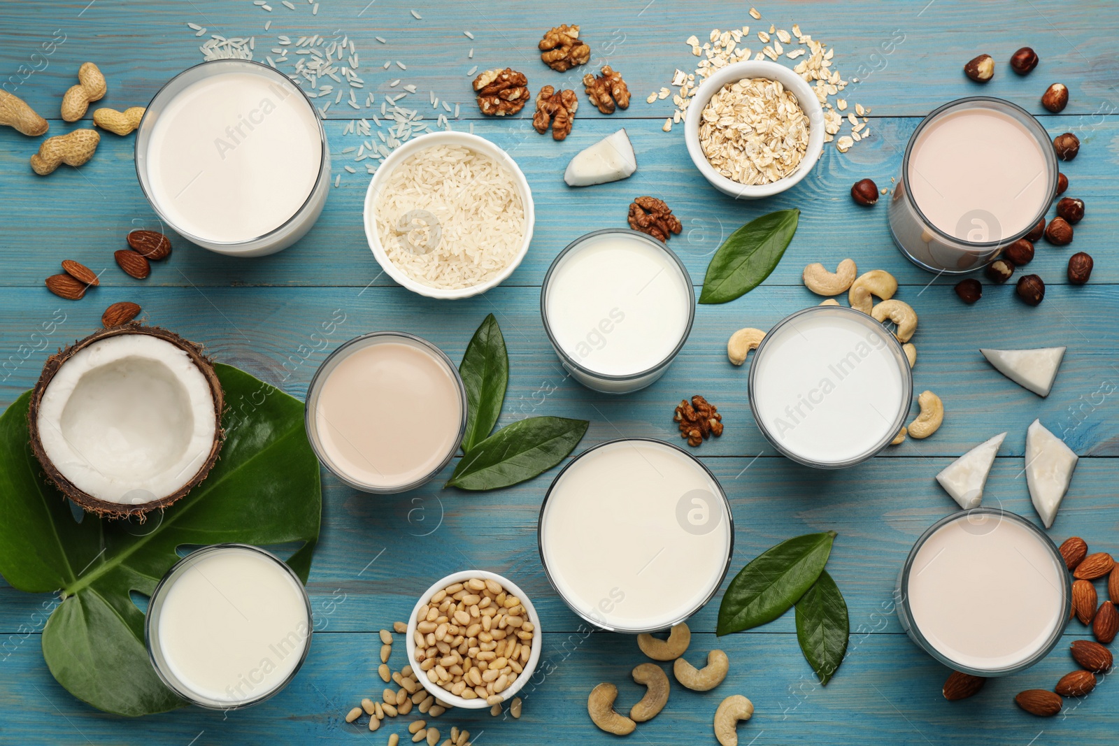 Photo of Different organic vegan milks and ingredients on light blue wooden table, flat lay