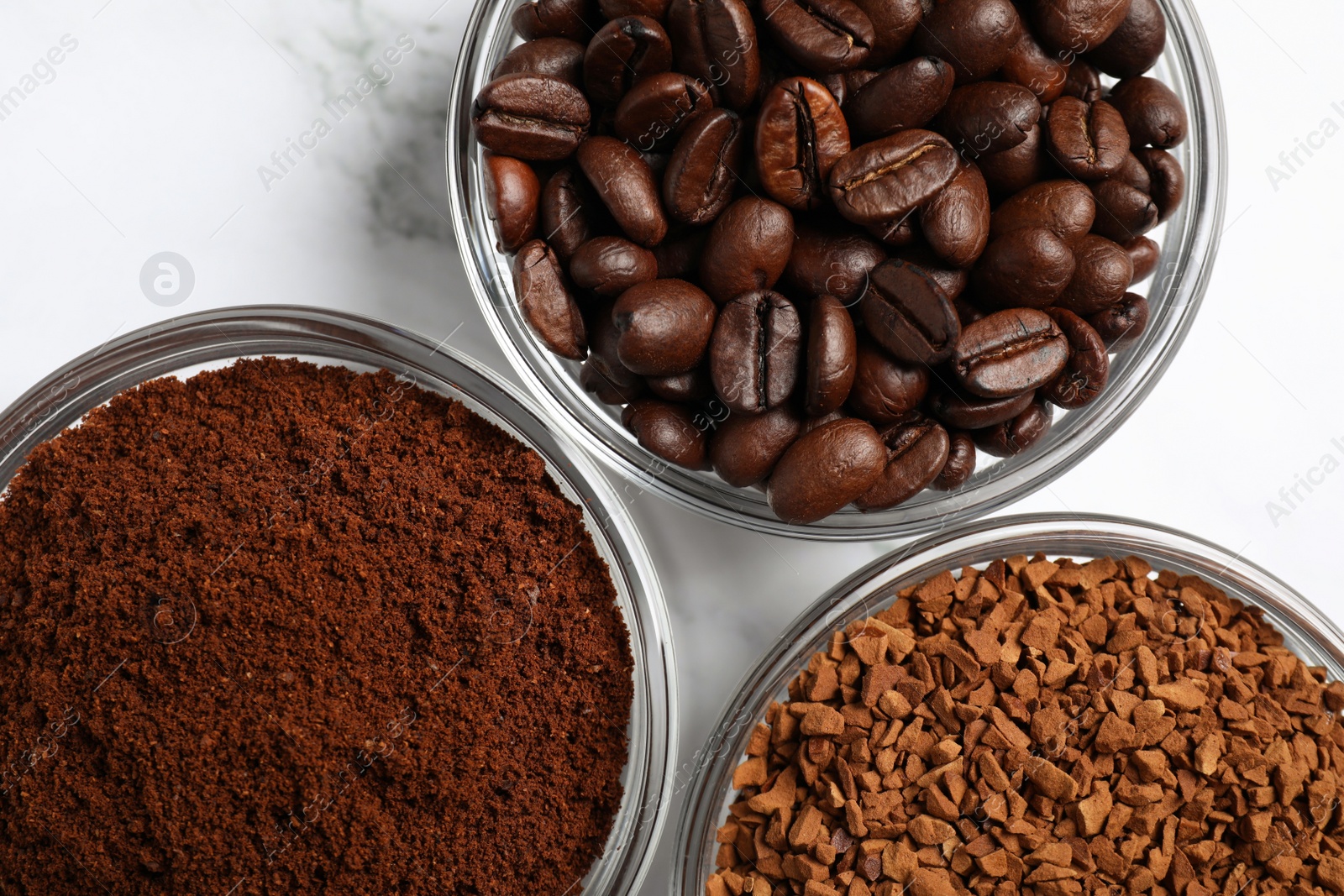 Photo of Bowls of beans, instant and ground coffee on white marble table, flat lay