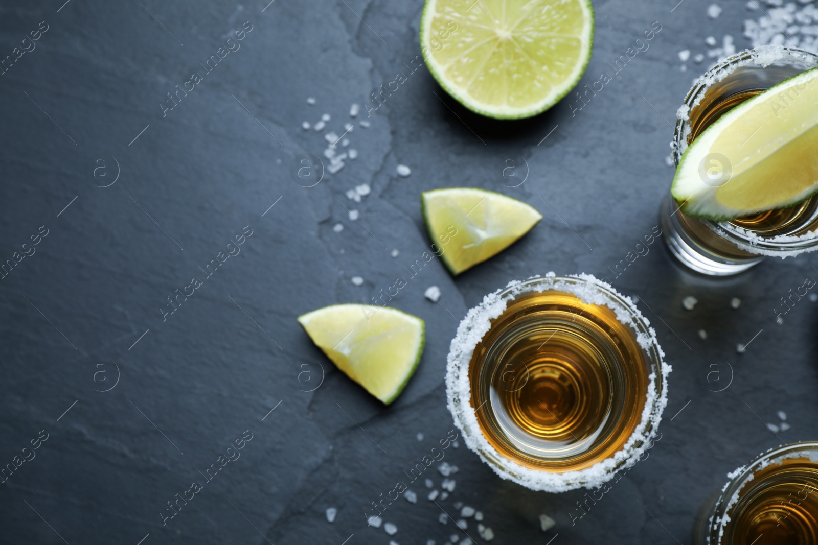 Photo of Mexican Tequila shots with salt and lime slices on grey table, flat lay. Space for text