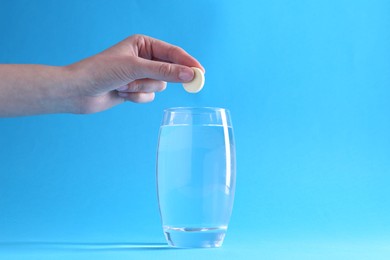 Woman putting effervescent pill into glass of water on light blue background, closeup