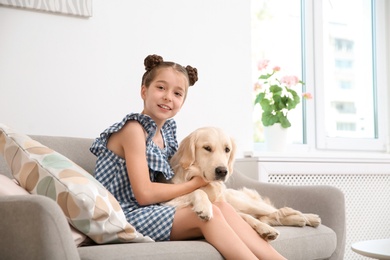 Cute little child with her pet on sofa at home