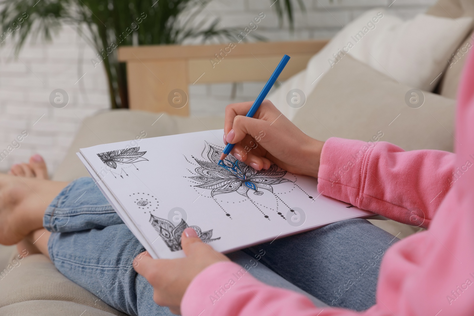 Photo of Young woman coloring antistress page on sofa in living room, closeup