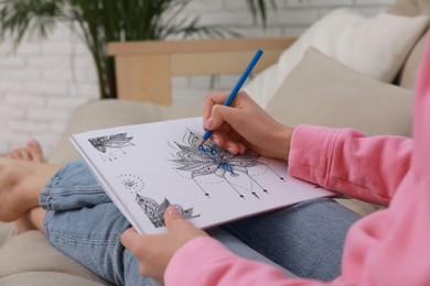 Young woman coloring antistress page on sofa in living room, closeup