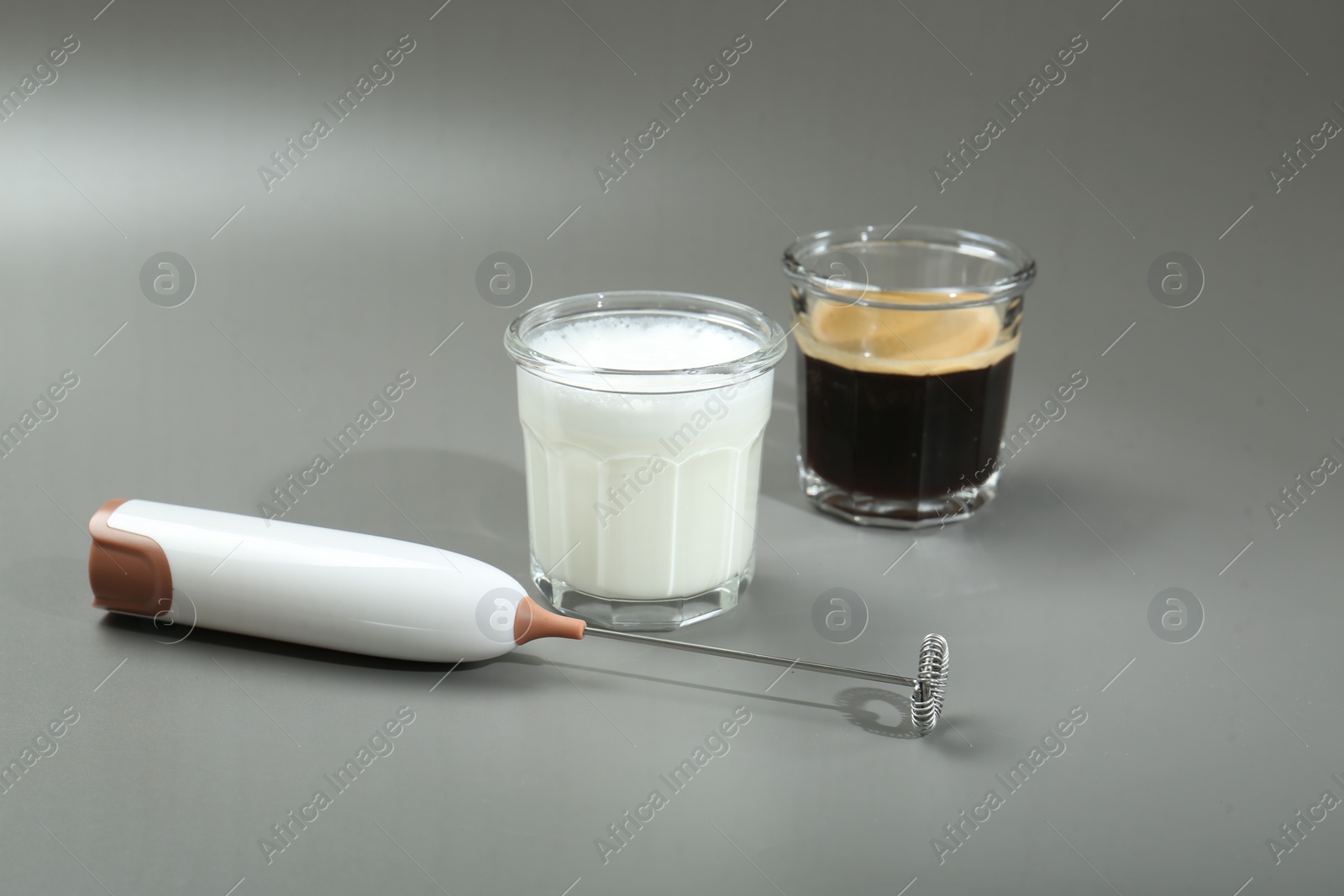 Photo of Mini mixer (milk frother), coffee and milk in glasses on grey background