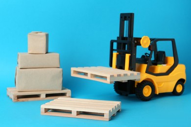 Photo of Toy forklift, wooden pallets and boxes on light blue background