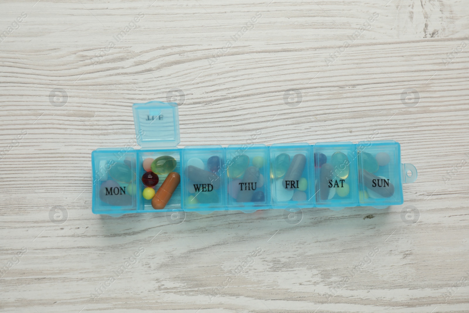 Photo of Plastic box with different pills on wooden table, top view