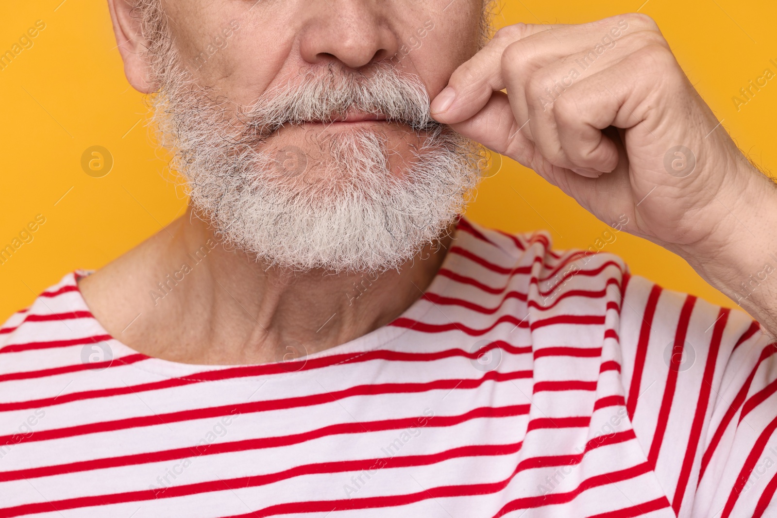 Photo of Man touching mustache on orange background, closeup