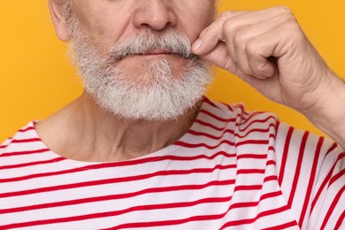 Man touching mustache on orange background, closeup
